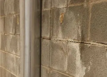 Basement wall showing cracks alongside a vertical metal pipe, highlighting potential structural issues relevant to foundation repair and carbon fiber reinforcement solutions.