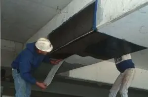 Technicians installing carbon fiber reinforcement sheet on concrete foundation beam