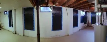 Basement walls with carbon fiber reinforcement, showcasing black patches on white concrete, indicating foundation repair solutions for structural stability.