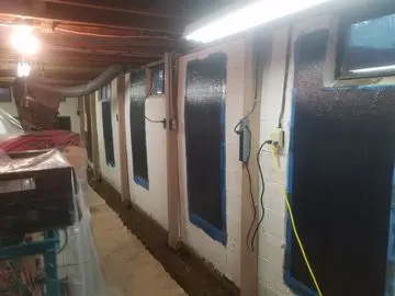 Basement walls treated with carbon fiber reinforcement technology, showcasing black application areas and blue painter's tape, illustrating foundation repair techniques.