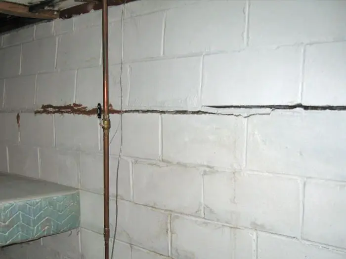Bowing foundation wall with visible step cracks and copper piping in a basement setting, illustrating signs of structural damage and the need for professional repair.