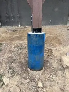 Carbon fiber structural support column installation, featuring a blue cylindrical base and wooden beam connection, showcasing StablWall's reinforcement solutions in construction.