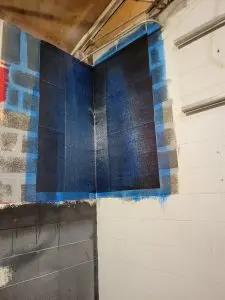Corner wrap reinforcement installation on a foundation wall, featuring blue protective coating and visible cinder block structure, illustrating StablWall's foundation repair solutions.