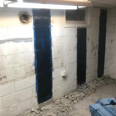 Foundation repair in progress with StablWall's structural strengthening system applied to cracked basement walls, showcasing vertical blue strips on cinder block walls and a partially cleared floor.