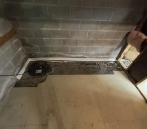 Interior basement waterproofing system with sump pump and perimeter drainage channel installed along foundation wall.