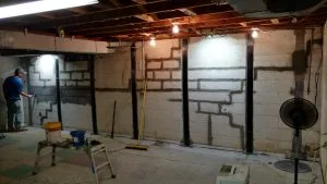Foundation repair contractor installing carbon fiber reinforcement straps on basement walls to stabilize structural movement.