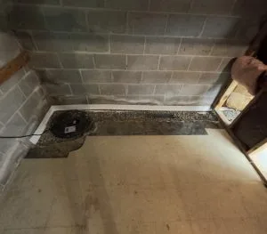 Interior basement waterproofing system with sump pump and perimeter drainage channel installed along foundation wall.