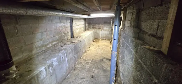 Damp basement in Elmore, OH with visible water stains along concrete walls and floor before waterproofing