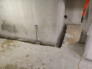 Basement wall with visible mold growth and water damage, excavation area for structural reinforcement, shovel leaning against wall, signs of moisture intrusion in Waterville, OH home.