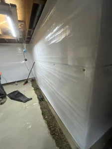 Installation of ThermalShield&trade; wall vapor barrier in a basement, showcasing moisture protection and energy efficiency features, with clean concrete floor and construction tools visible.