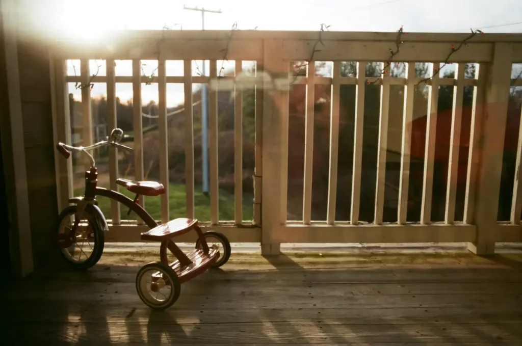 Deck design ideas for small yards featuring a compact wooden deck with railing and a child’s tricycle at sunset