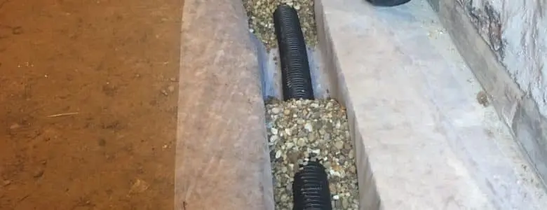 Interior basement waterproofing system with drainage trench, gravel, and corrugated pipe installation