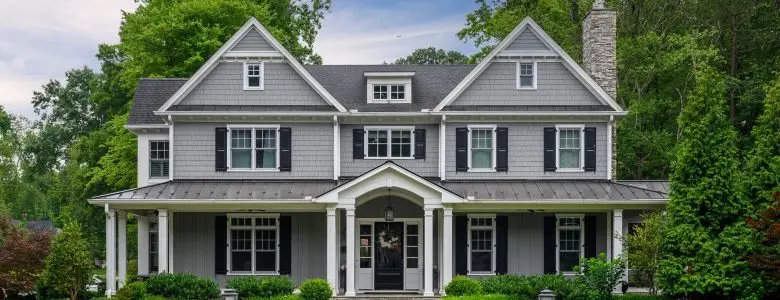 Gray colonial-style house with white trim, two stories, and stone chimney. Manicured lawn with stone path and lanterns. Lush trees surround the home, in Fort Hunt VA