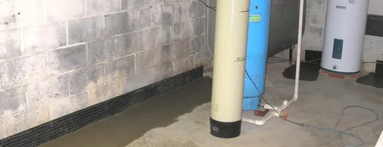 DIY basement waterproofing area with drainage system and water treatment equipment along a concrete block wall