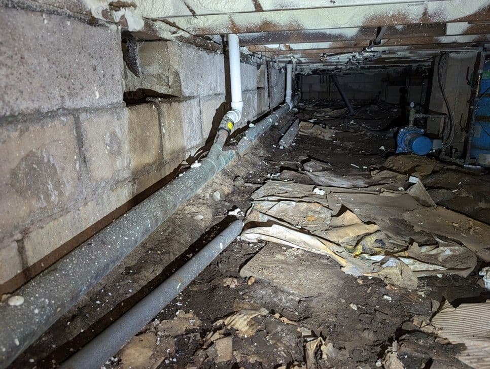Damp crawlspace with exposed soil, debris, and plumbing showing moisture problems before professional crawlspace encapsulation.