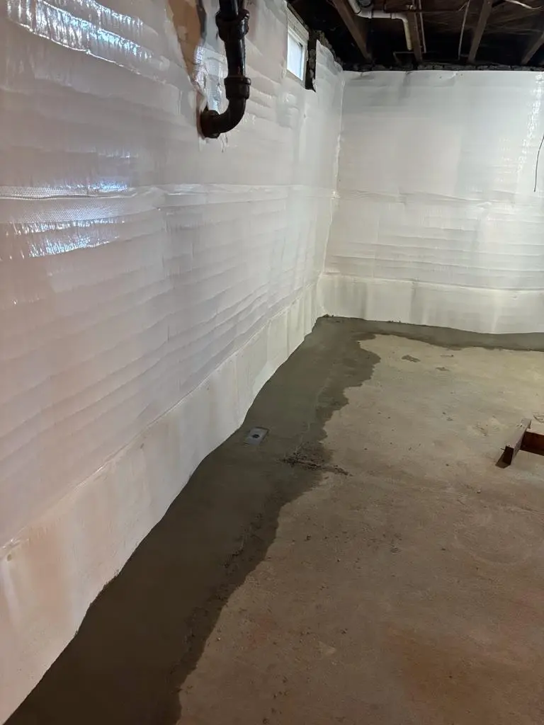 Completed full-perimeter Grate Drain waterproofing system installed in a Norwich, CT basement with wall protection and restored concrete floor.