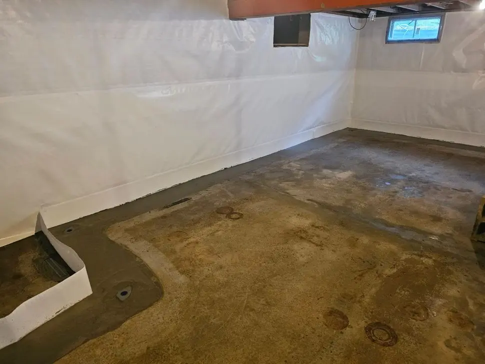 Interior perimeter drainage system installed along a basement wall before concrete restoration to prevent flooding and relieve hydrostatic pressure.
