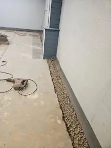 Interior basement waterproofing system installation showing a perimeter drainage trench with clean gravel before the concrete floor is restored.