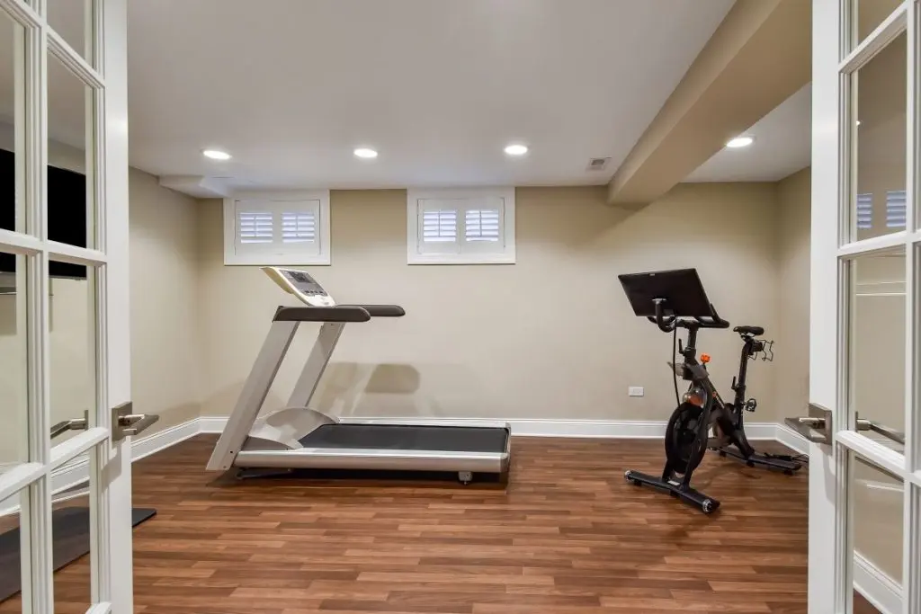 Home gym featuring a treadmill and stationary bike in a well-lit basement with improved air quality, emphasizing the benefits of EZ Breathe ventilation for healthier living spaces.