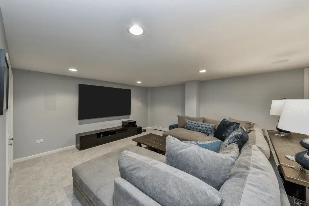 Cozy finished basement TV room featuring plush seating, modern decor, and a large flat-screen TV, illustrating the importance of ventilation in remodeled below-grade spaces.