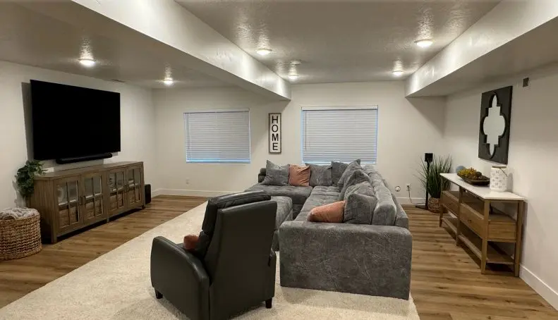 Modern basement living room featuring a sectional sofa, large TV, and decorative elements, emphasizing the importance of ventilation for indoor air quality.