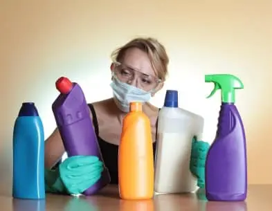 Person wearing protective gear examining various cleaning products, emphasizing the importance of proper ventilation and indoor air quality in basements and crawlspaces.