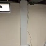 EZ Breathe ventilation system installed in a basement, featuring a tall, white unit against a light-colored wall, with visible electrical wiring, illustrating improvements in indoor air quality.