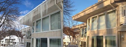 Residential building with icicles hanging from the roof, illustrating ice dam formation, surrounded by snow-covered landscape, relevant to ice dam prevention strategies.