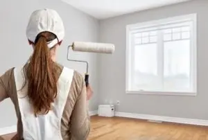 Person holding a paint roller in a freshly painted gray room, emphasizing indoor air quality and the importance of low and no VOC paints.