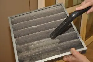Dirty air filter being cleaned with a vacuum to improve indoor air quality and prevent musty odors in homes.