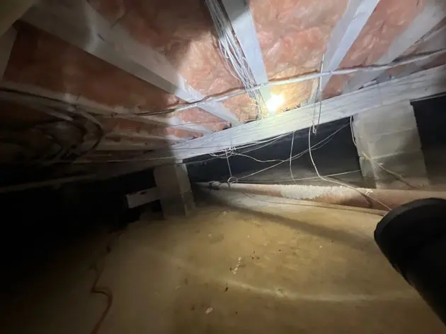 Crawl space interior with exposed insulation, wires, and a dim light, highlighting potential moisture issues related to home health in New Jersey.