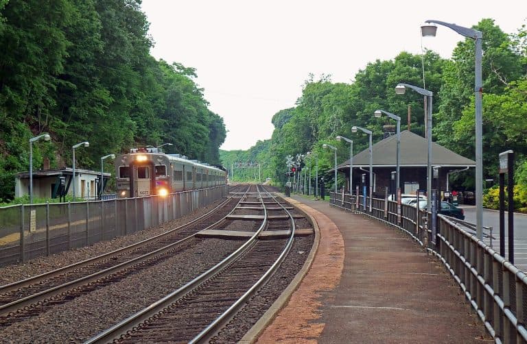 Train approaching Ho-Ho-Kus NJ Transit station, surrounded by greenery and station infrastructure, emphasizing local transportation accessibility for homeowners seeking waterproofing solutions.