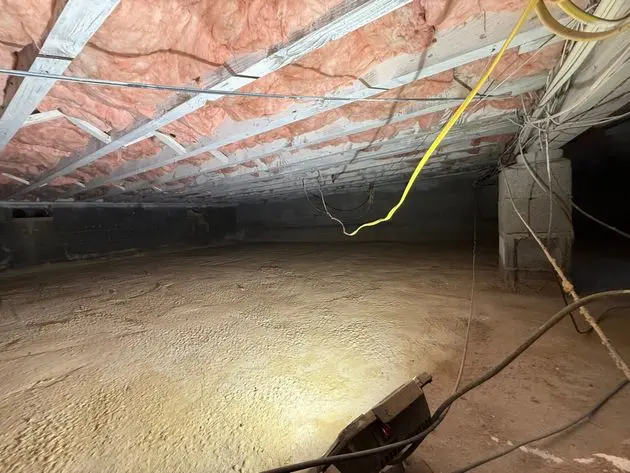 Unencapsulated crawl space in a New Jersey home with exposed soil, fiberglass insulation between floor joists, and concrete block foundation walls.