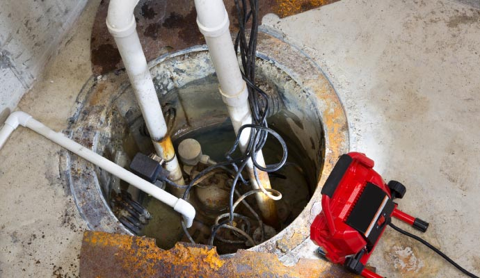 Sump pump system in a basement, featuring pipes, electrical wiring, and a red pump, illustrating essential water management for preventing basement flooding and water damage.