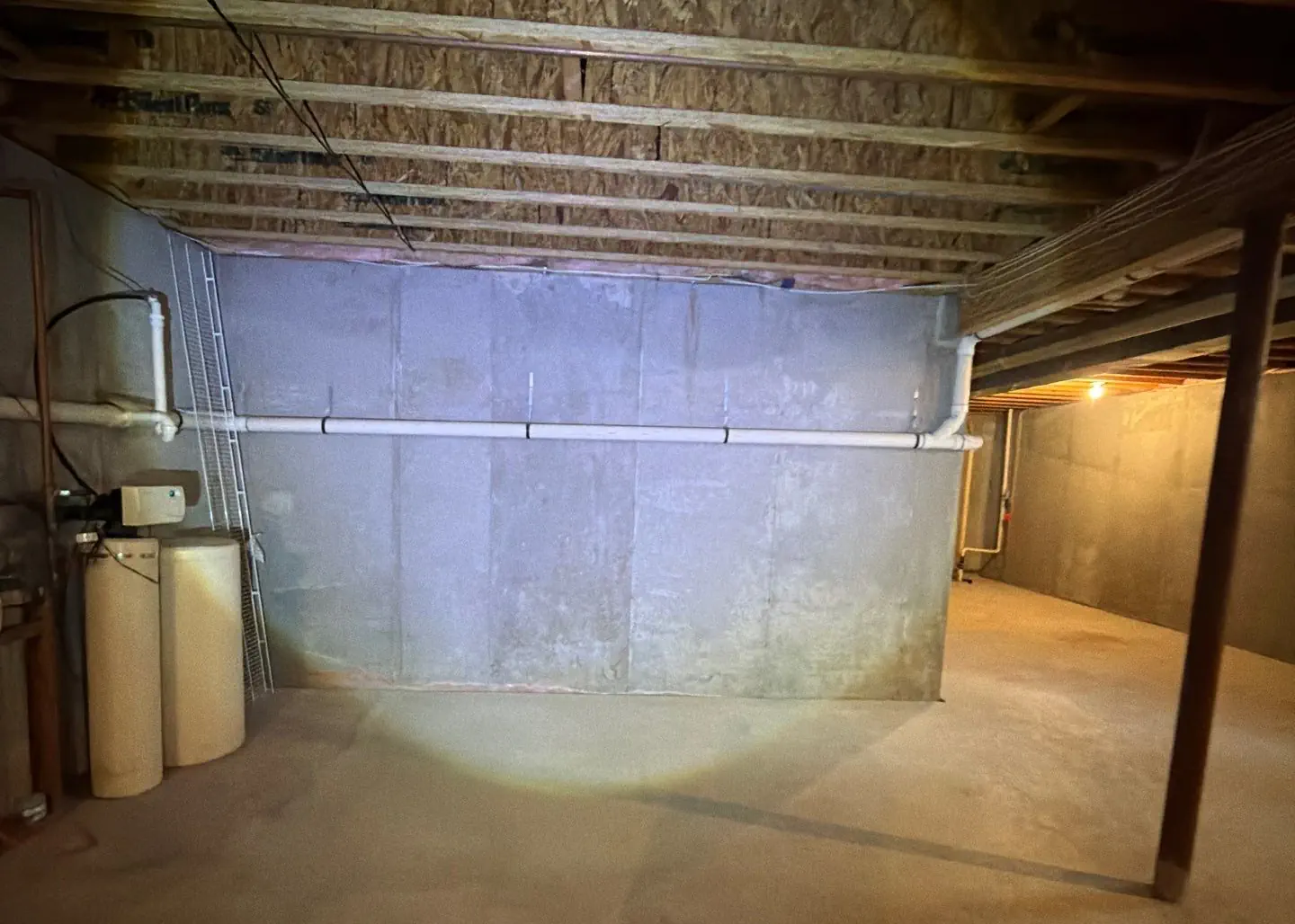 Basement interior in Monrow Township with exposed beams, concrete walls, and plumbing fixtures, showcasing recent waterproofing work by Healthy Way Waterproofing & Mold Remediation.