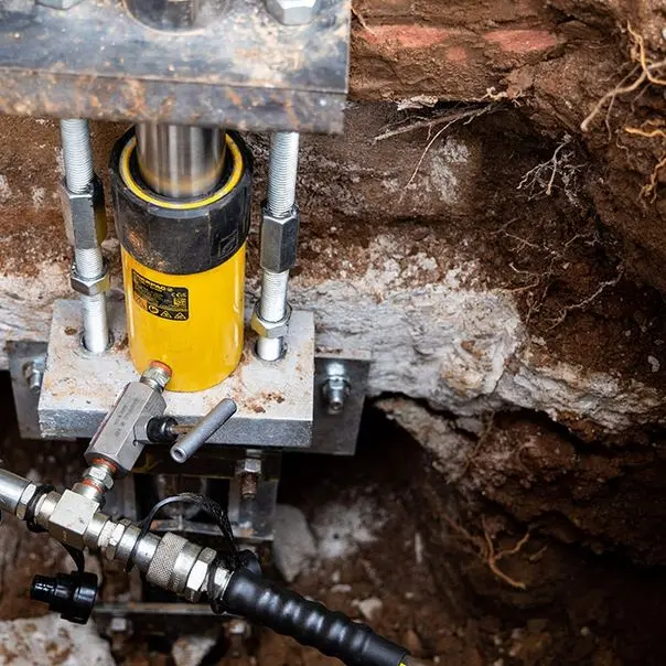 Foundation repair process with hydraulic jack supporting cracked foundation wall in Kentucky.