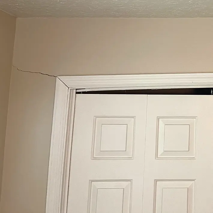 Cracked wall and door frame indicating foundation issues and structural damage.
