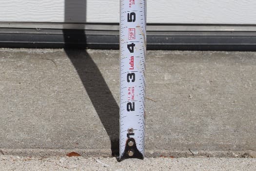 Uneven driveway surface with measuring tape showing height difference, driveway leveling solution.