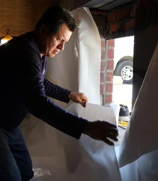 Foundation Solutions Group technician waterproofing a basement with plastic sheeting.