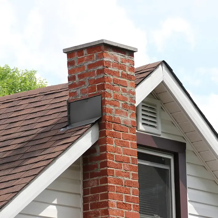 Leaning brick chimney on a house roof, indicating potential foundation issues.