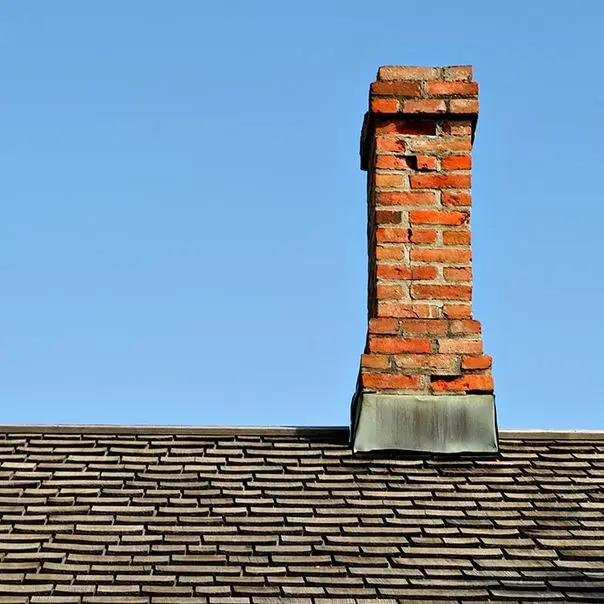 Leaning brick chimney on a house roof, sign of potential foundation settlement and structural damage.