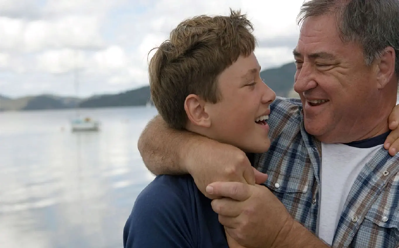 A man and boy are hugging near the water.