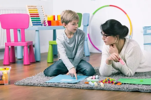 A woman and boy sitting on the floor playing with toys.