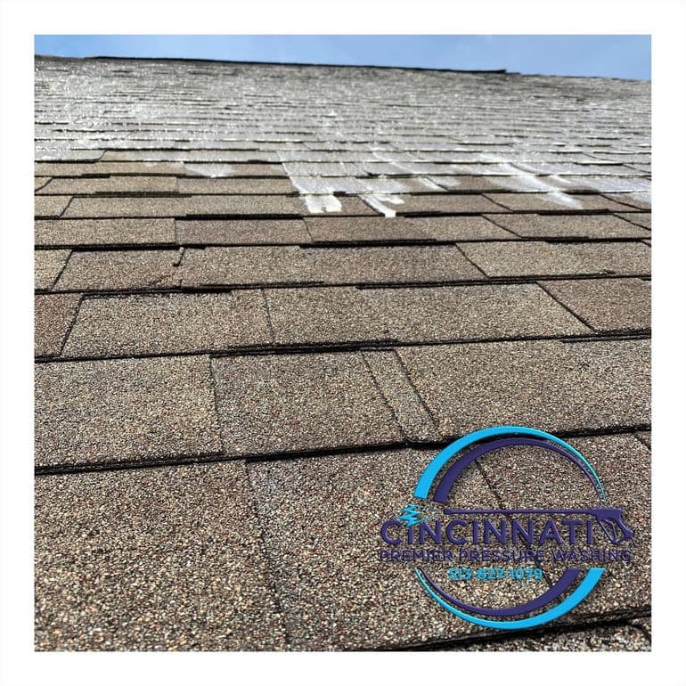 Close-up of a shingle roof during a cleaning process, showing a clear contrast between treated and untreated areas, with Cincinnati Premier Pressure Washing logo at the bottom