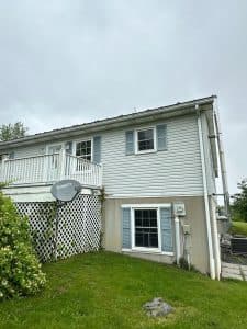 pro pressure works cleaning a light blue vinyl siding with green grass and a lattice fence in the foreground