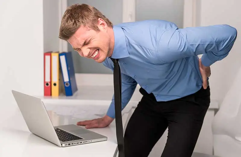 Man experiencing lower back pain while working at laptop, seeking pain relief at McCracken Chiropractic.