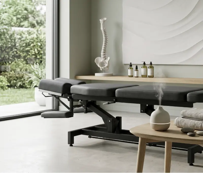 Chiropractic treatment table in a modern, serene setting, with a spinal model and essential oils,