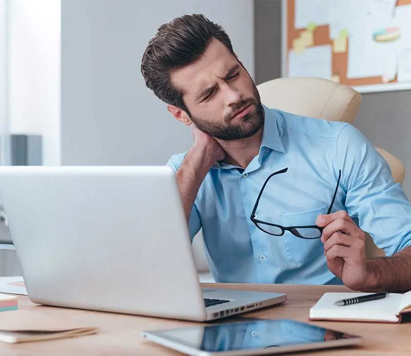 Man with neck pain and poor posture working at a laptop.
