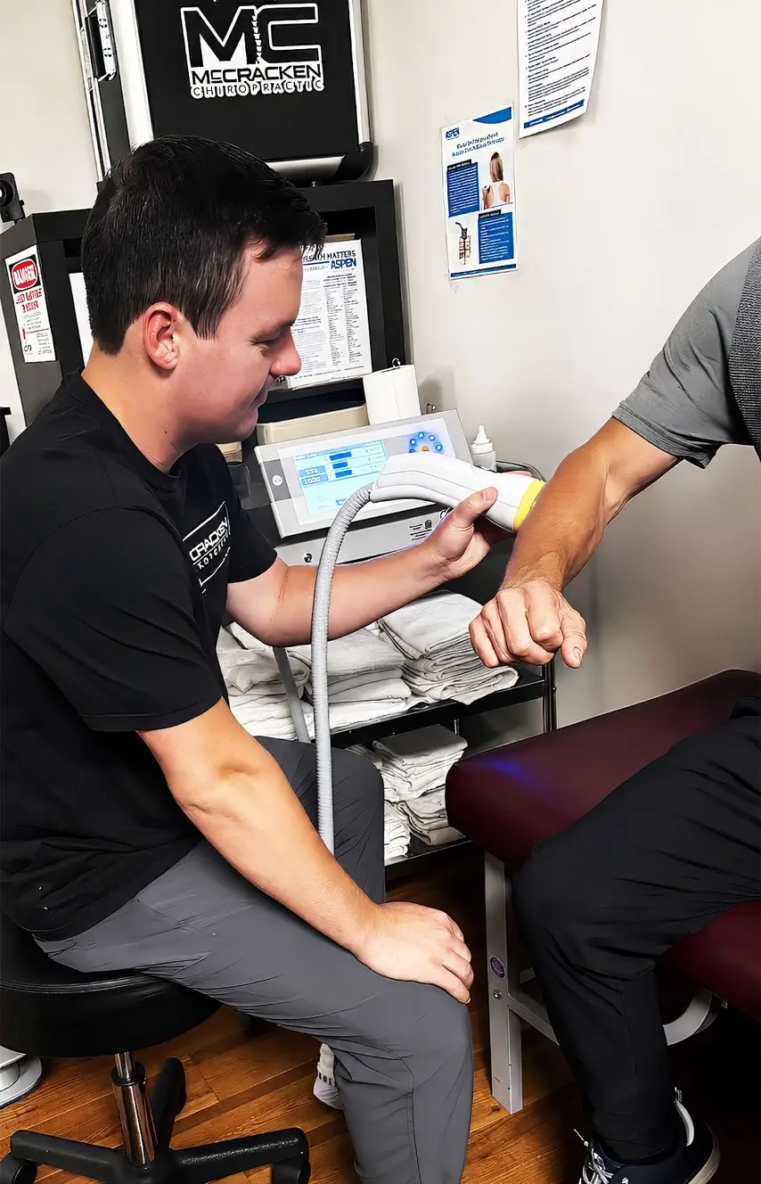 Chiropractic specialist treating a patient's arm with a SoftWave therapy device on an examination table.