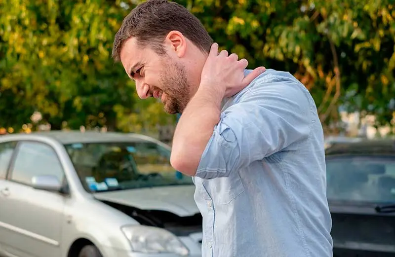 Man holding neck in pain near damaged car, illustrating whiplash and auto accident injuries.